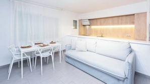 Uma kitchenette moderna e minimalista com forno embutido e pia, uma mesa de jantar branca com cadeiras e um sofá azul claro.