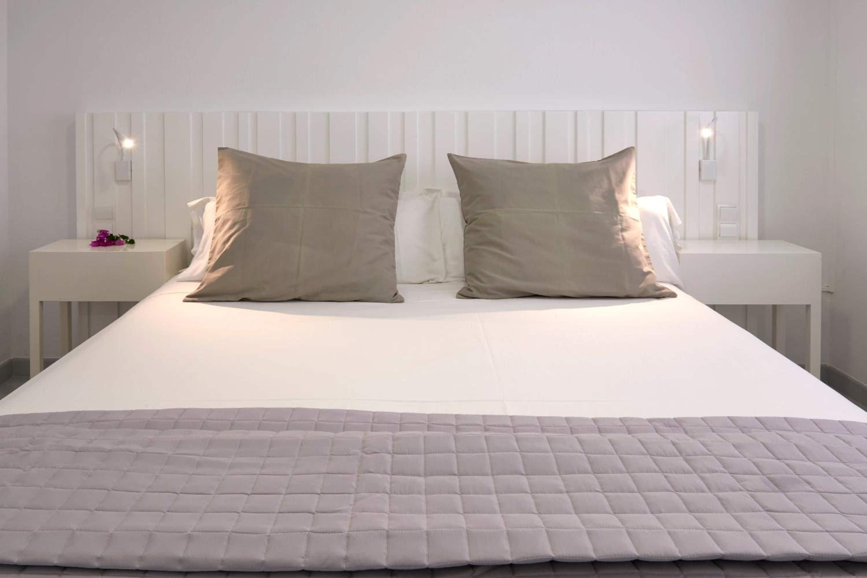 Una cama bien hecha con cubrecama acolchado, dos mesitas de noche con lámparas y un cabecero blanco.