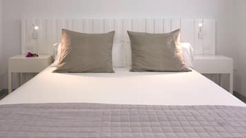 Una cama bien hecha con cubrecama acolchado, dos mesitas de noche con lámparas y un cabecero blanco.