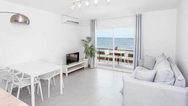 A modern living room with a dining area, a TV, and a view of the sea. - Enkala Apartamentos (Ibiza Town)