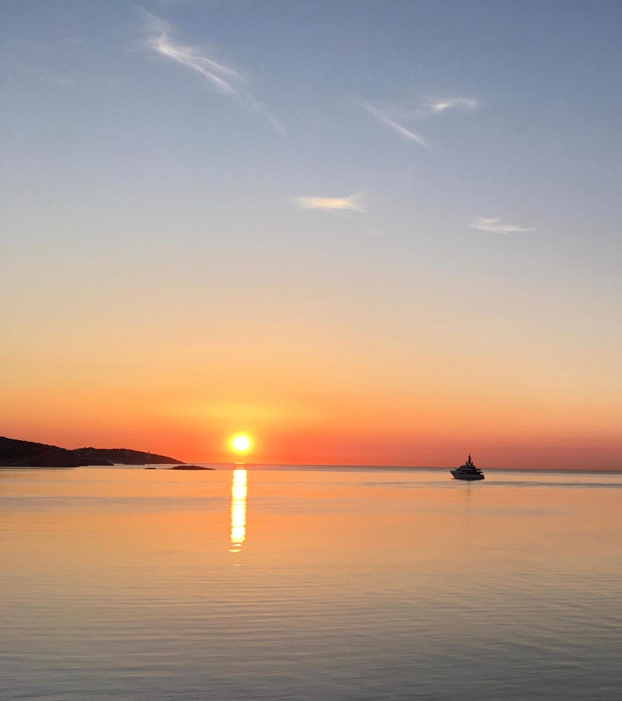 Ein ruhiges Meer bei Sonnenuntergang, im Hintergrund ein Boot.
