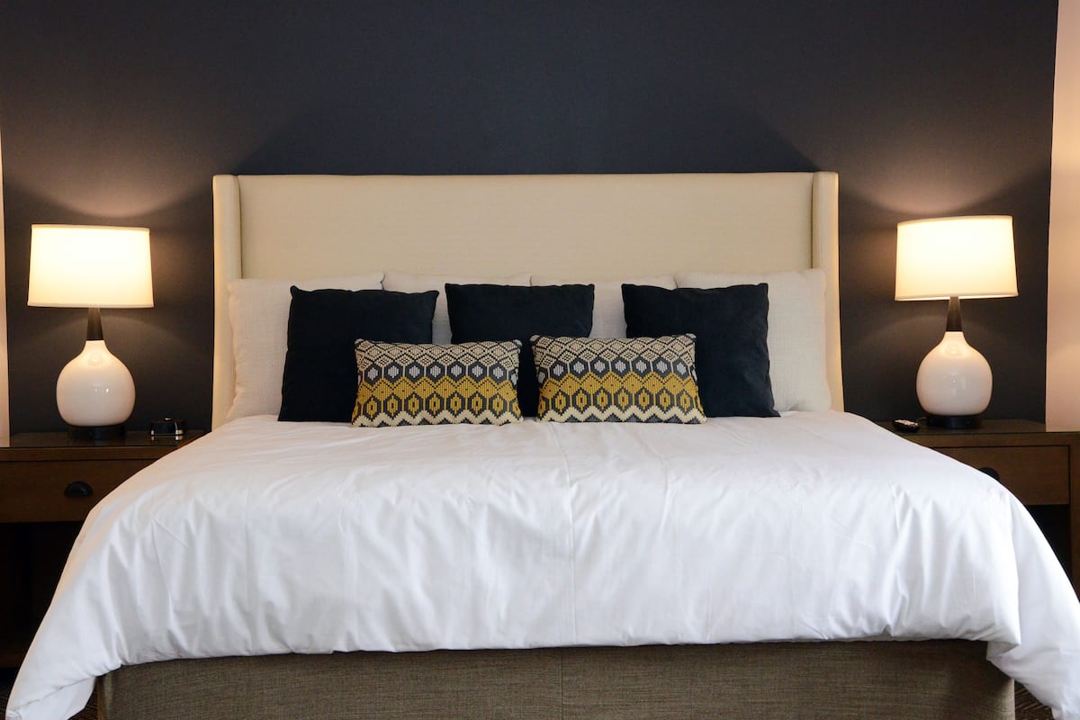 A neatly made bed with white bedding and patterned pillows, flanked by two bedside lamps on matching nightstands.