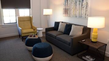 A living room with a sofa, armchair, ottoman, and a small side table with a lamp.