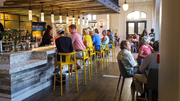 Zona de bar con mostrador, taburetes amarillos y un grupo de personas sentadas.