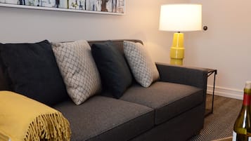 Un canapé gris avec des coussins à motifs, un plaid jaune et une lampe jaune.