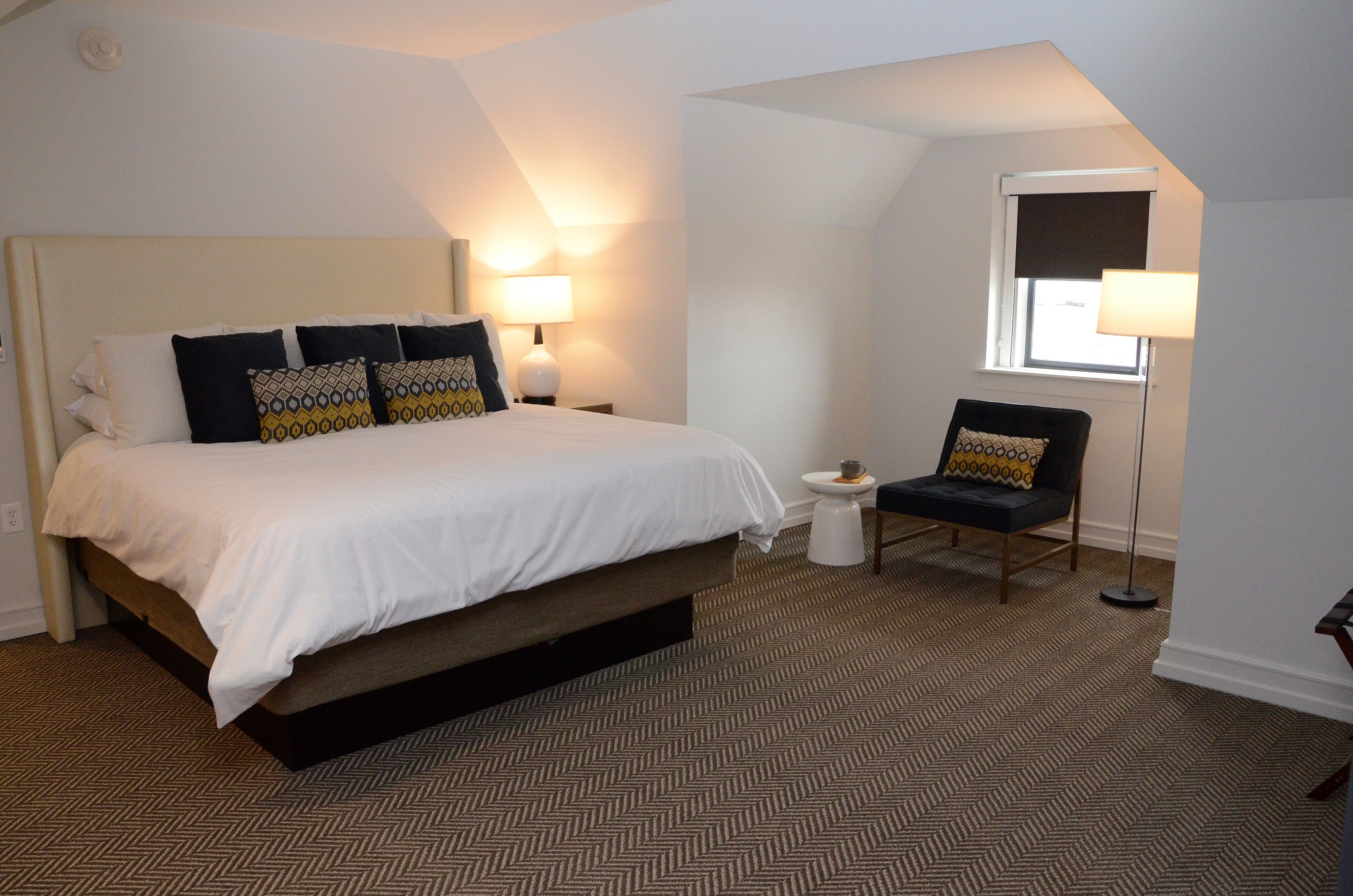 A bedroom with a large bed, two bedside lamps, a chair, and a small table.