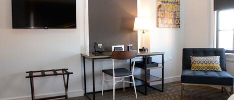 Habitación de hotel con televisión de pantalla plana, escritorio con silla, lámpara, sofá y alfombra estampada.