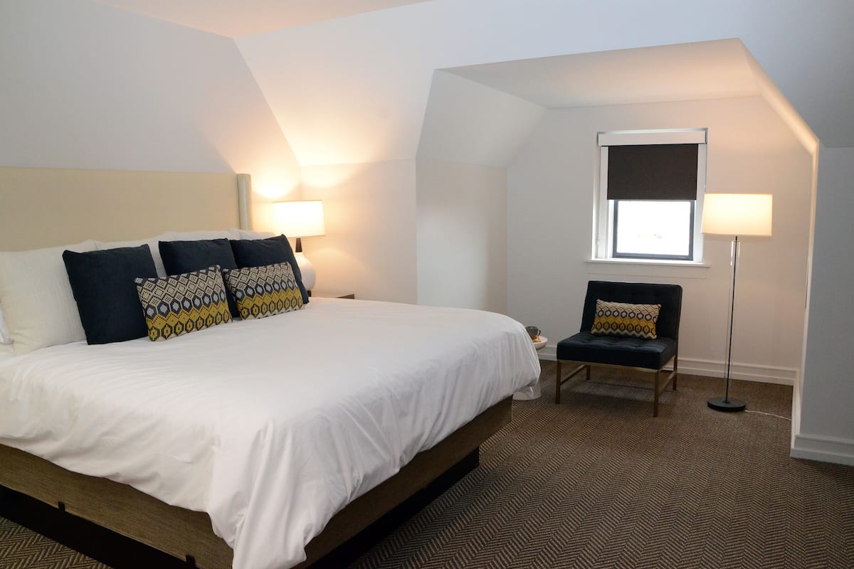 A bedroom with a bed, two bedside lamps, a chair, and a window.