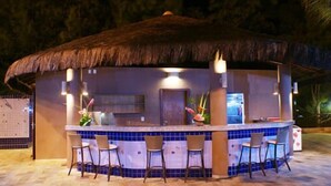 Un área de bar con techo de paja, mostrador de baldosas y taburetes.