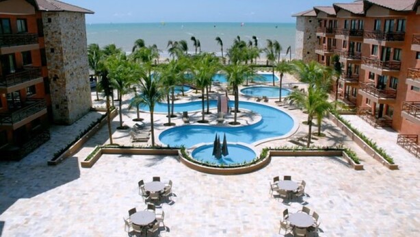 Un resort con varias piscinas, palmeras y vista a la playa.