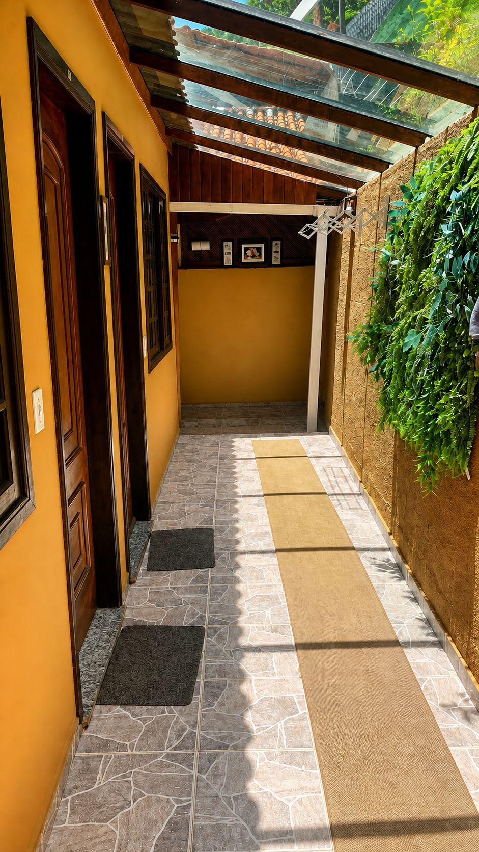 Un couloir étroit doté d’un sol carrelé, de portes en bois, d’un plafond en verre et d’un mur recouvert d’une plante grimpante.