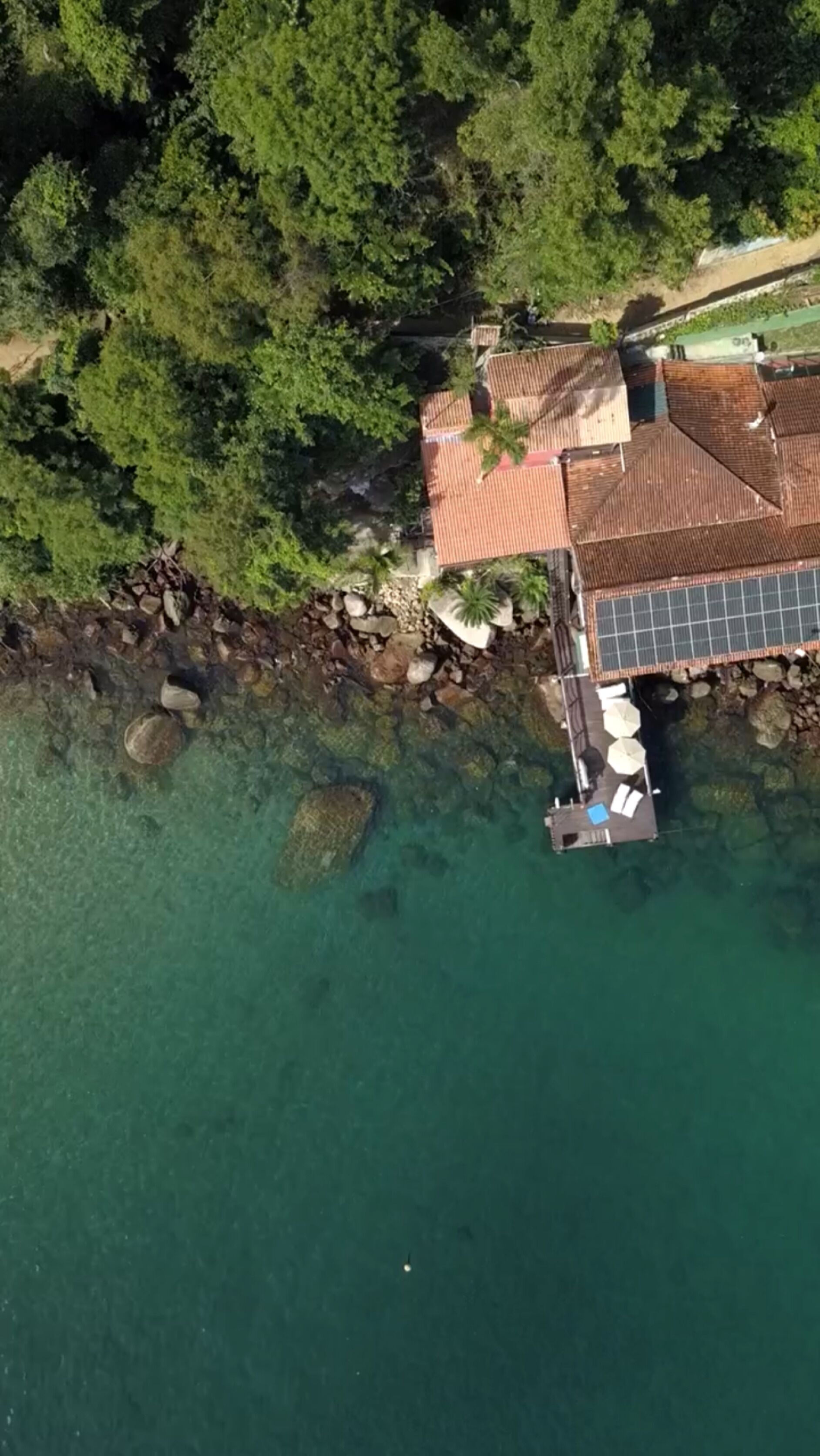 Luftaufnahme eines Küsteneigentums mit einem Haus, einem Steg und klarem türkisblauem Wasser.
