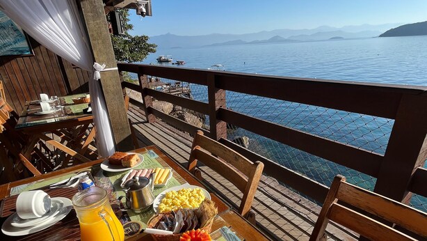 A breakfast table with various foods and a view of the sea. - Pousada Convés Ilha Grande (Angra dos Reis)