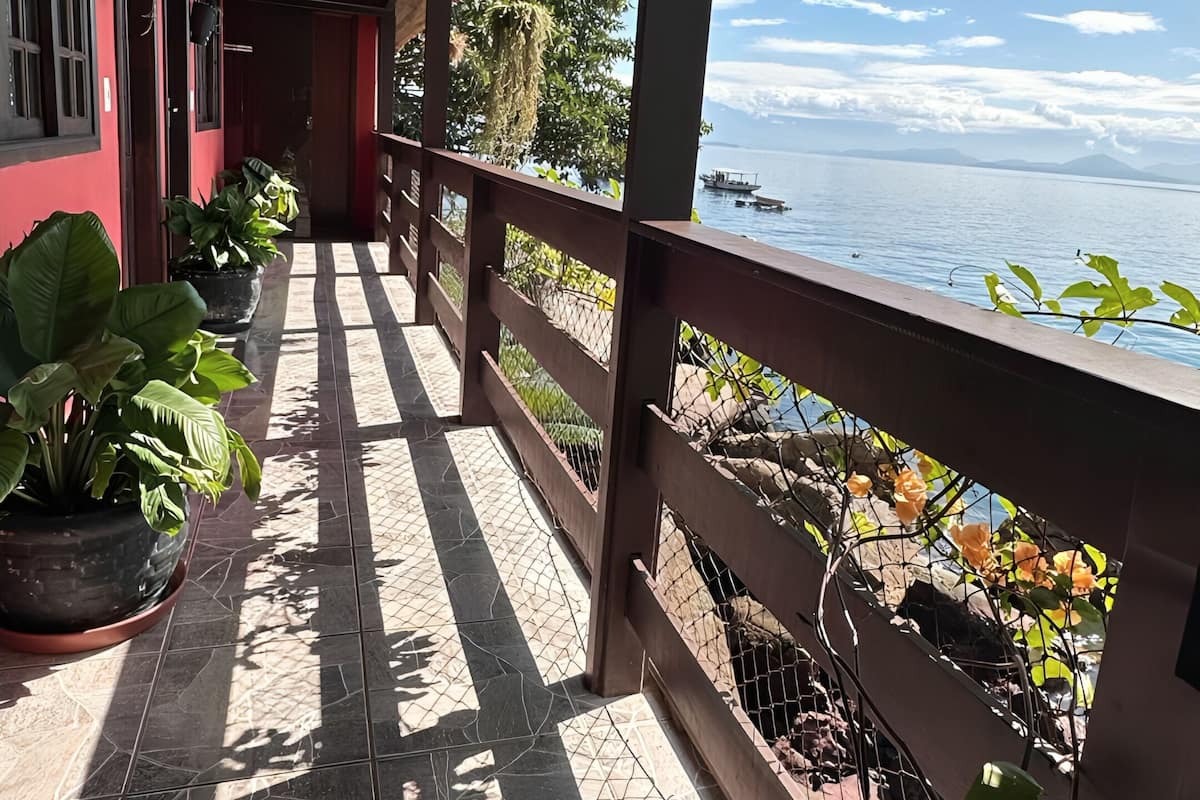 Une allée couverte agrémentée de plantes en pot, avec vue sur la mer et une rambarde en bois.