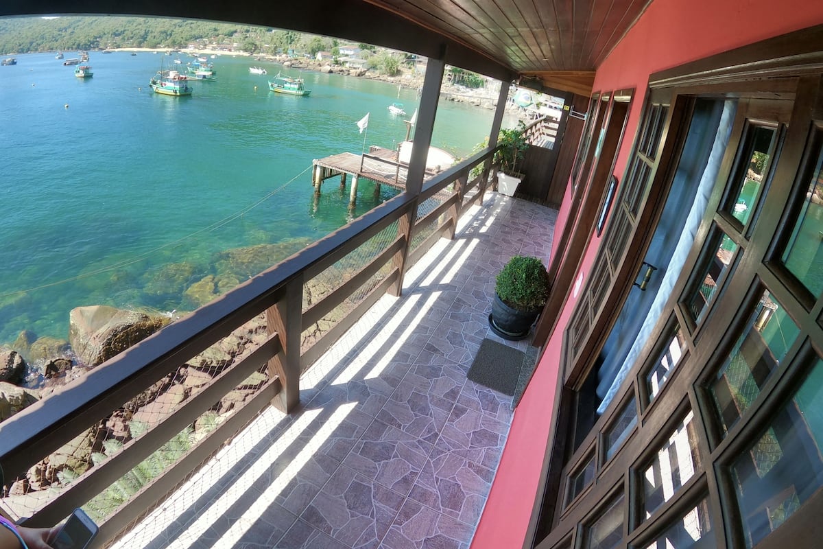 Un balcon donnant sur un plan d’eau calme où l’on peut admirer les bateaux, une terrasse en bois et un pot de fleurs.