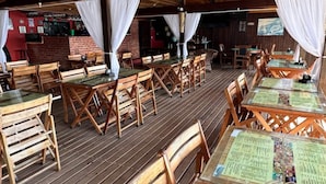 An outdoor restaurant with wooden tables and chairs, covered by a wooden roof with white drapes. - Pousada Convés Ilha Grande (Angra dos Reis)
