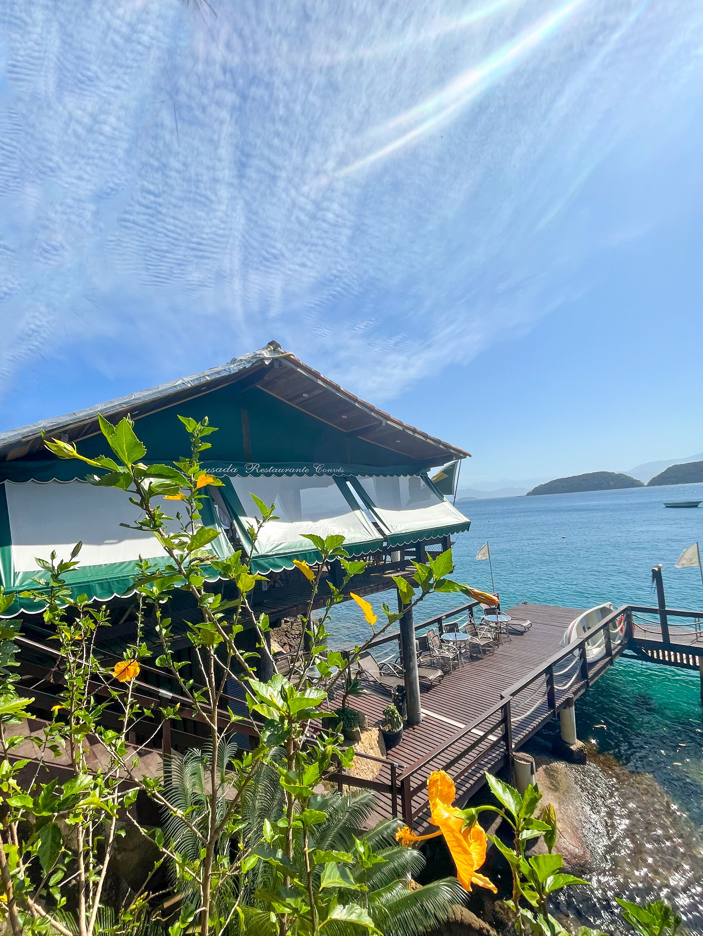 An overwater bungalows with a wooden deck and lounge chairs, overlooking a clear blue sea and distant islands.