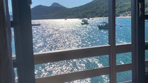 A view through a window with a wooden frame, overlooking a body of water with boats and a mountainous landscape. - Pousada Convés Ilha Grande (Angra dos Reis)