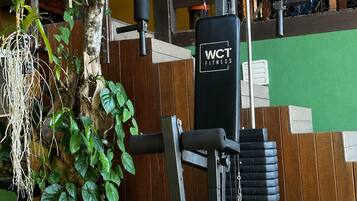 Uma academia com um banco de musculação, um saco de pancadas e diversas plantas.