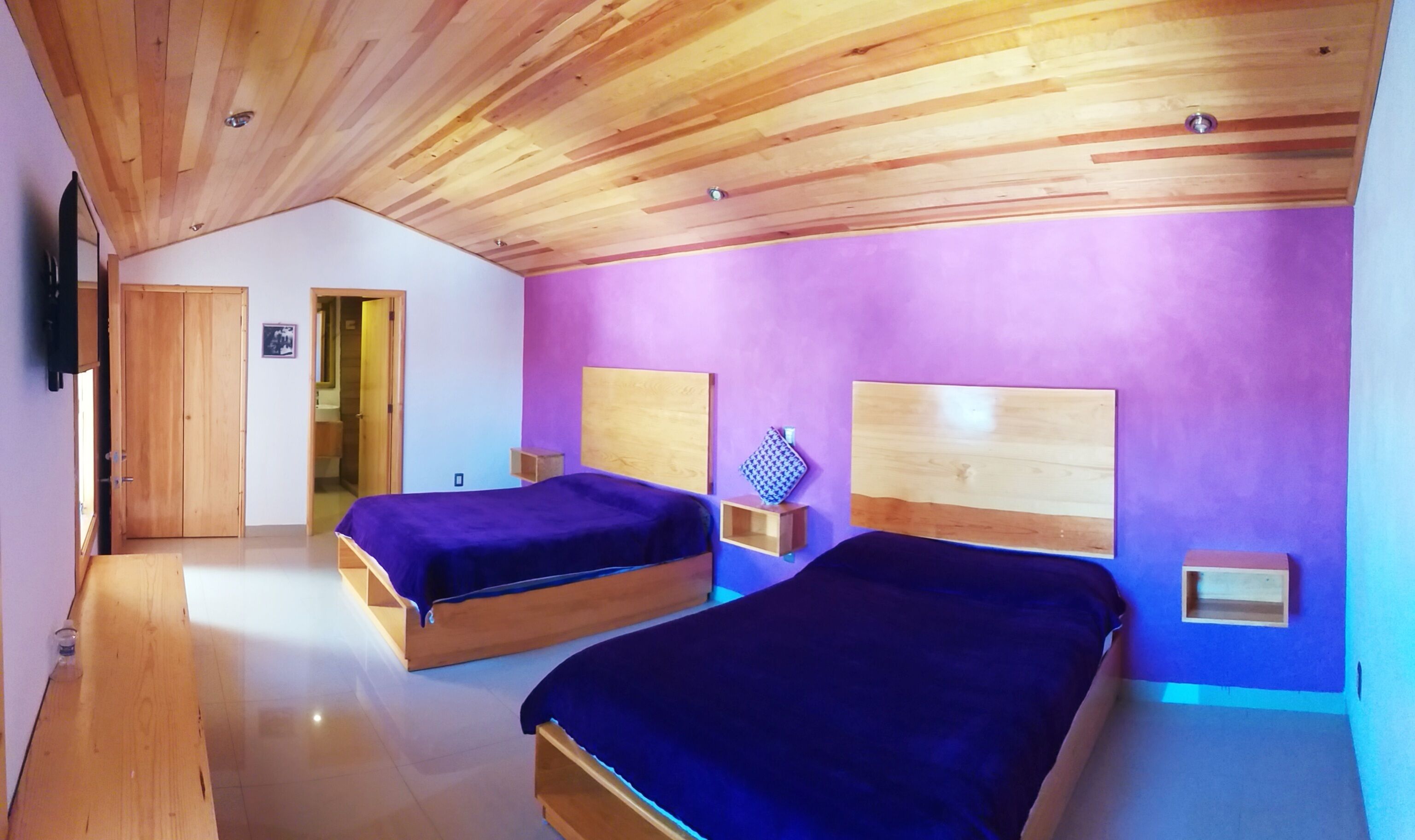 Un dormitorio con dos camas de madera, paredes moradas y techo de madera.