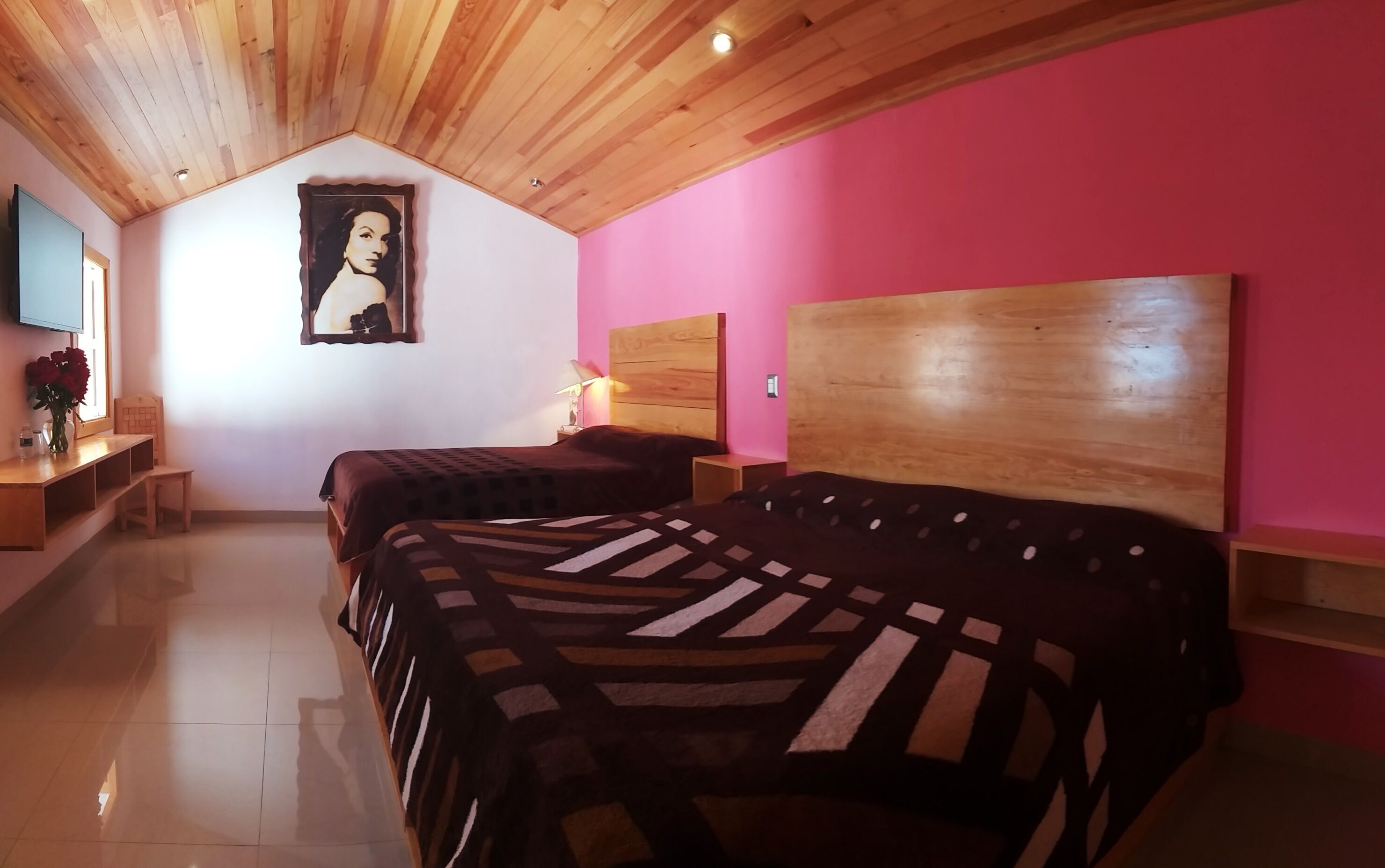 A bedroom with two beds, wooden ceiling, pink walls, and a framed portrait on the wall.