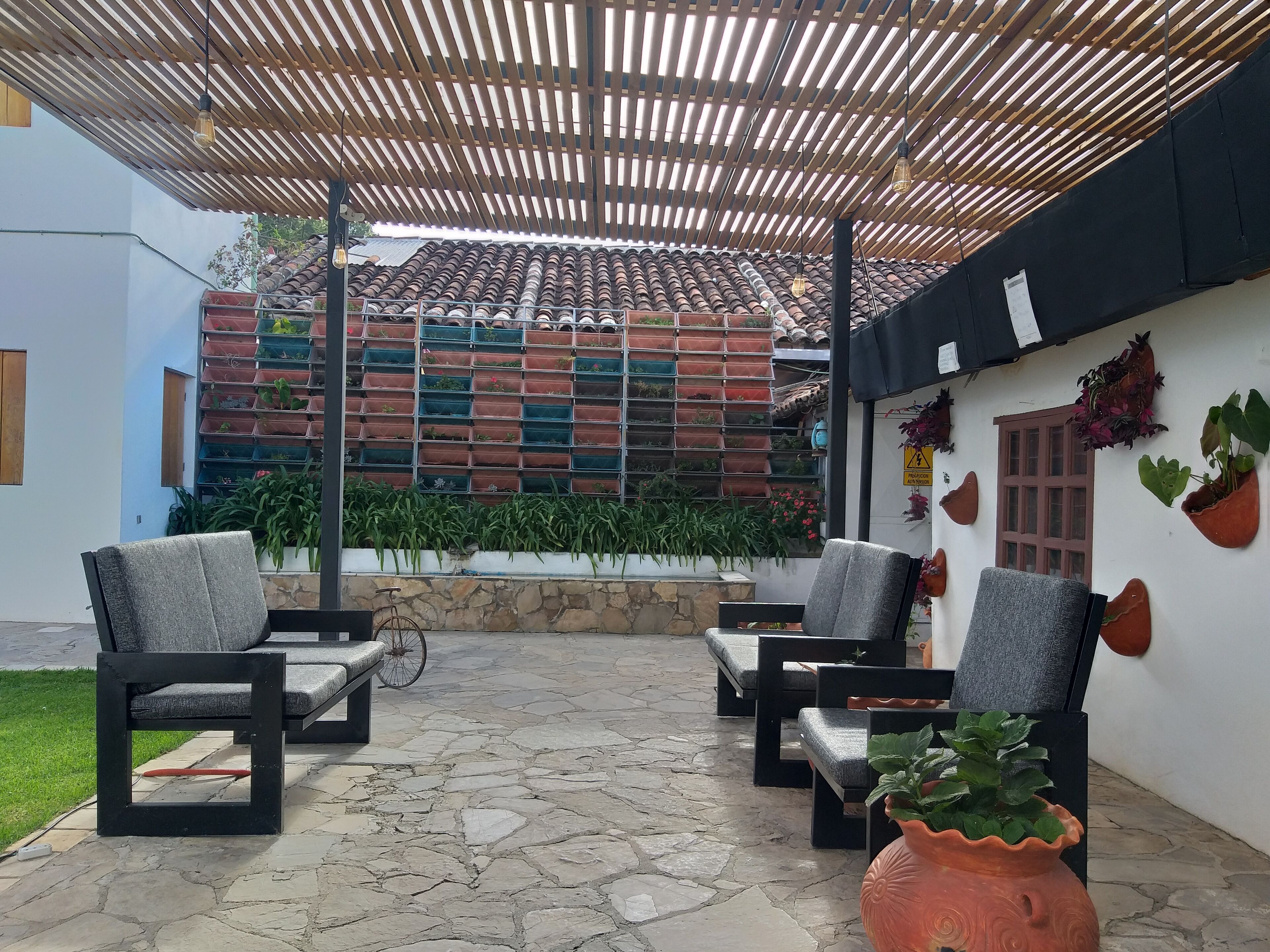 A covered outdoor seating area with stone flooring and chairs, a tiled roof, and potted plants.