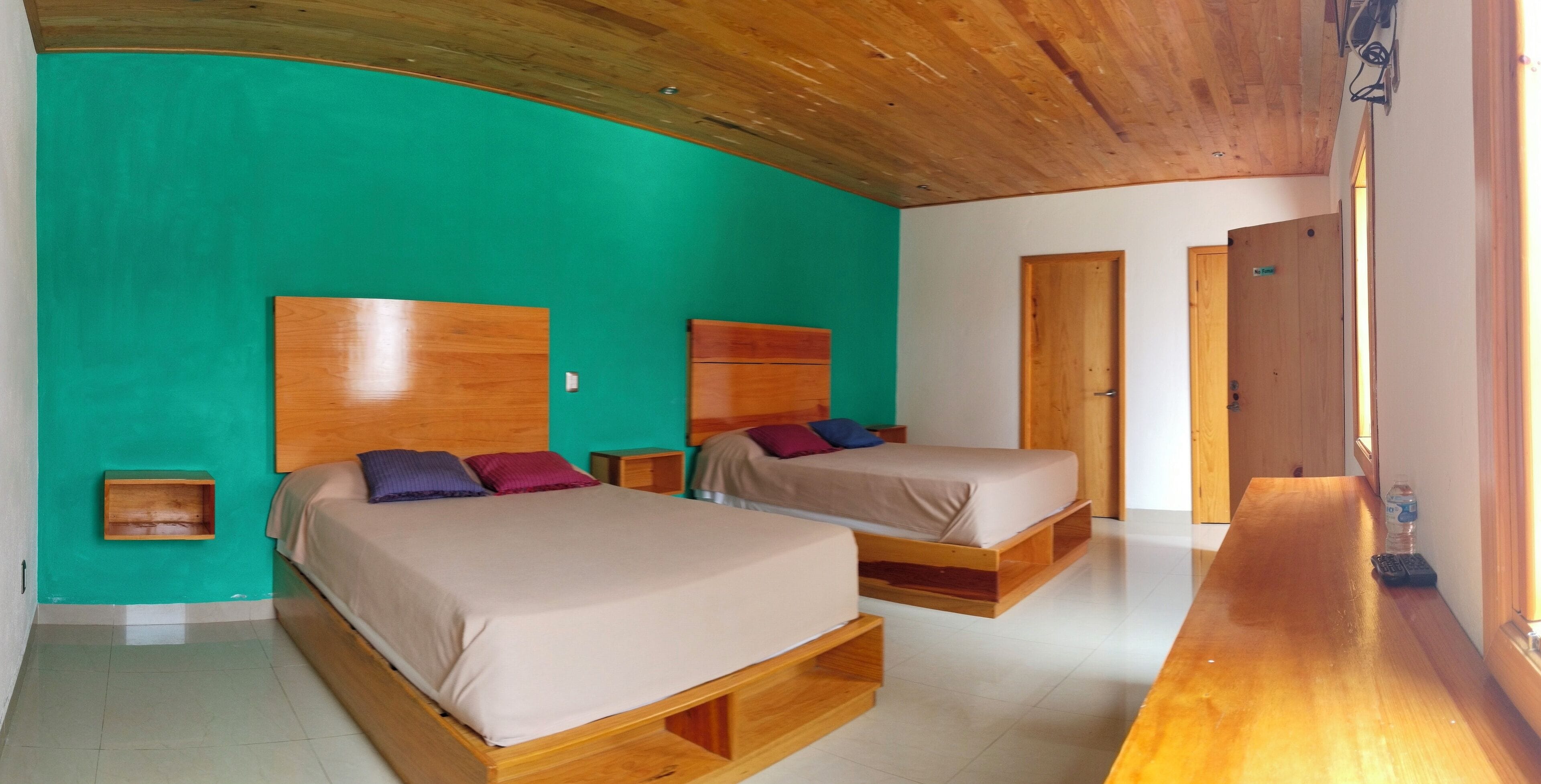 A room with two beds, a wooden bench, and a teal wall.