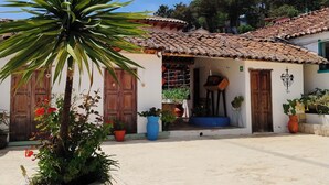 A courtyard with a large potted plant, a tiled-roof building, and a wooden door. - Hotel Yú (San Cristóbal de las Casas)