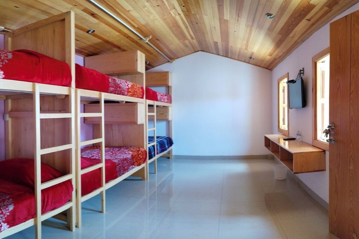 Habitación con literas de madera, un televisor en la pared y techo de madera.