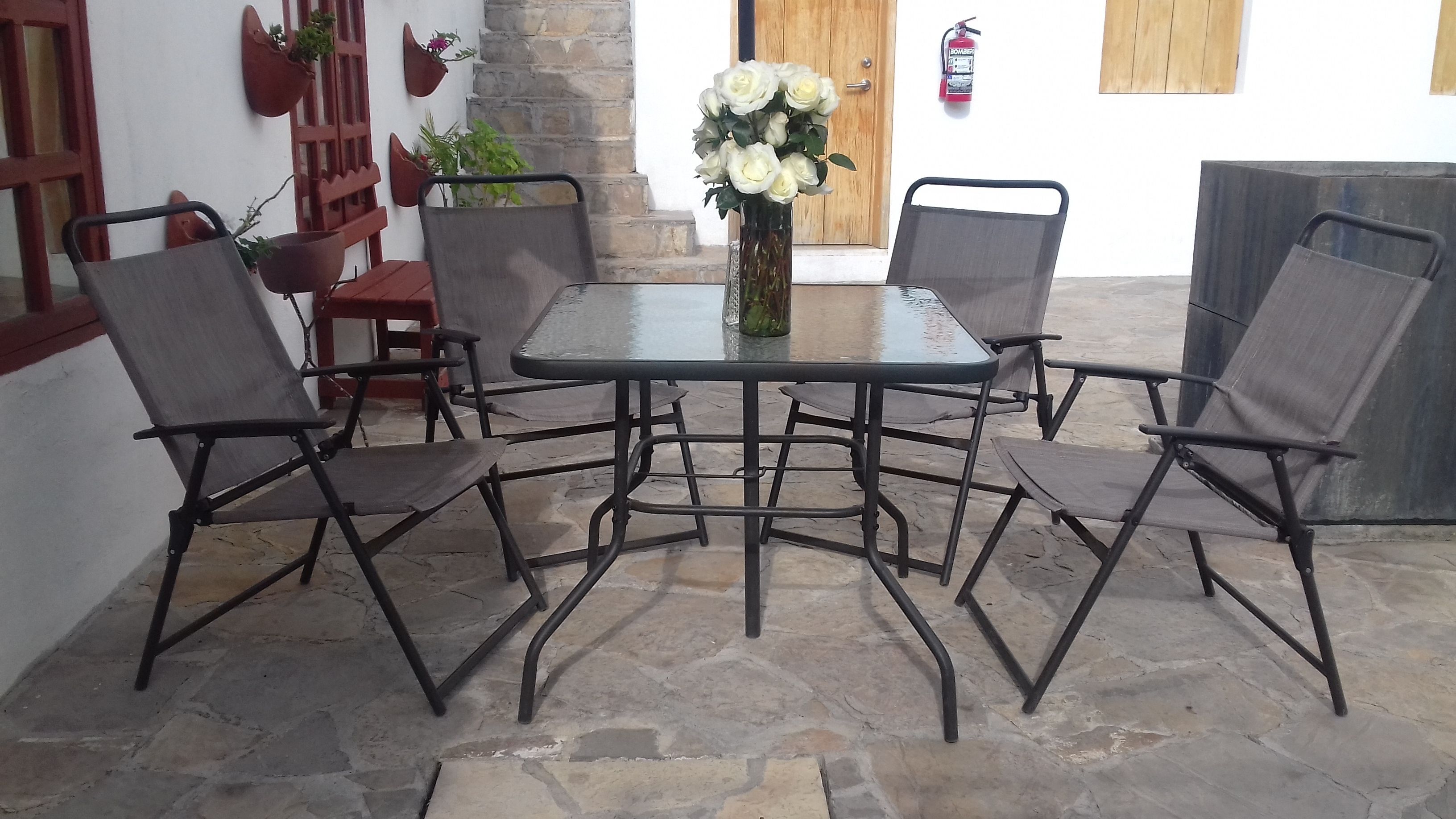 A patio with a table and chairs, a vase with flowers, and a fire extinguisher on the wall.