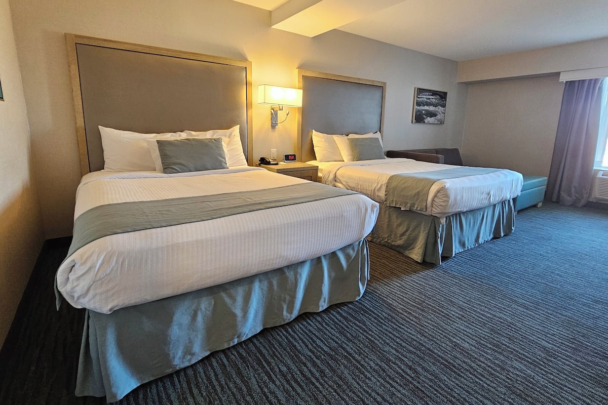 Ein Hotelzimmer mit zwei Betten, jeweils mit Kopfstütze, Nachttischen und Lampen.