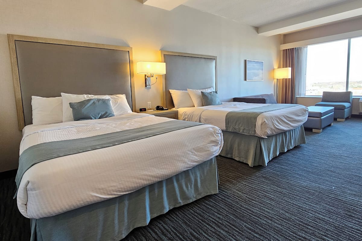 Ein Hotelzimmer mit zwei Betten, einem Schreibtisch, einem Stuhl und einem großen Fenster.