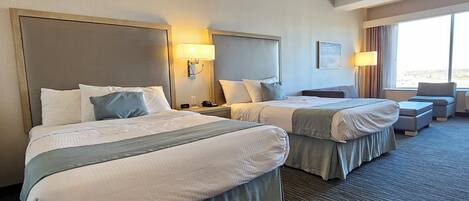 A hotel room with two beds, a desk, a chair, and a large window.