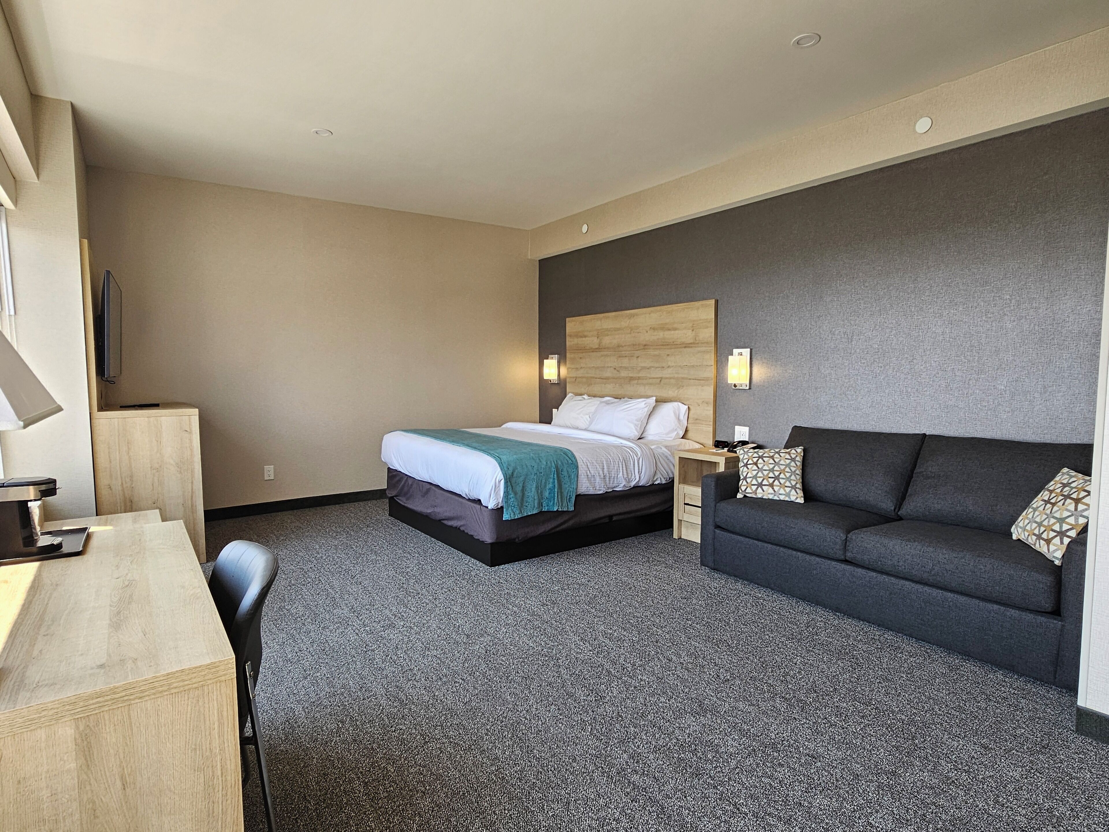 A hotel room with a bed, a desk, a sofa, and a TV.