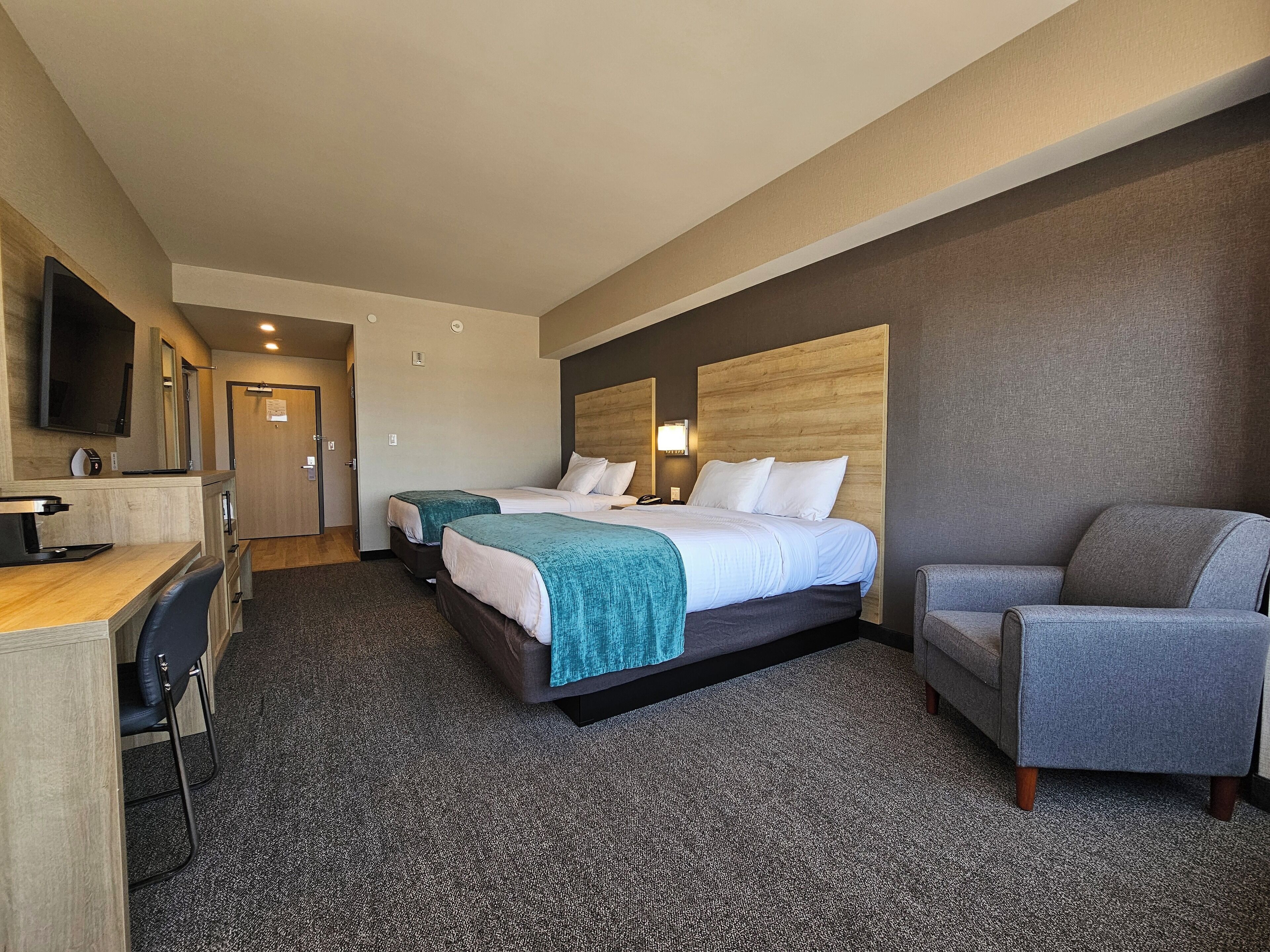 A hotel room with two beds, a desk with a chair, a TV, and a seating area.