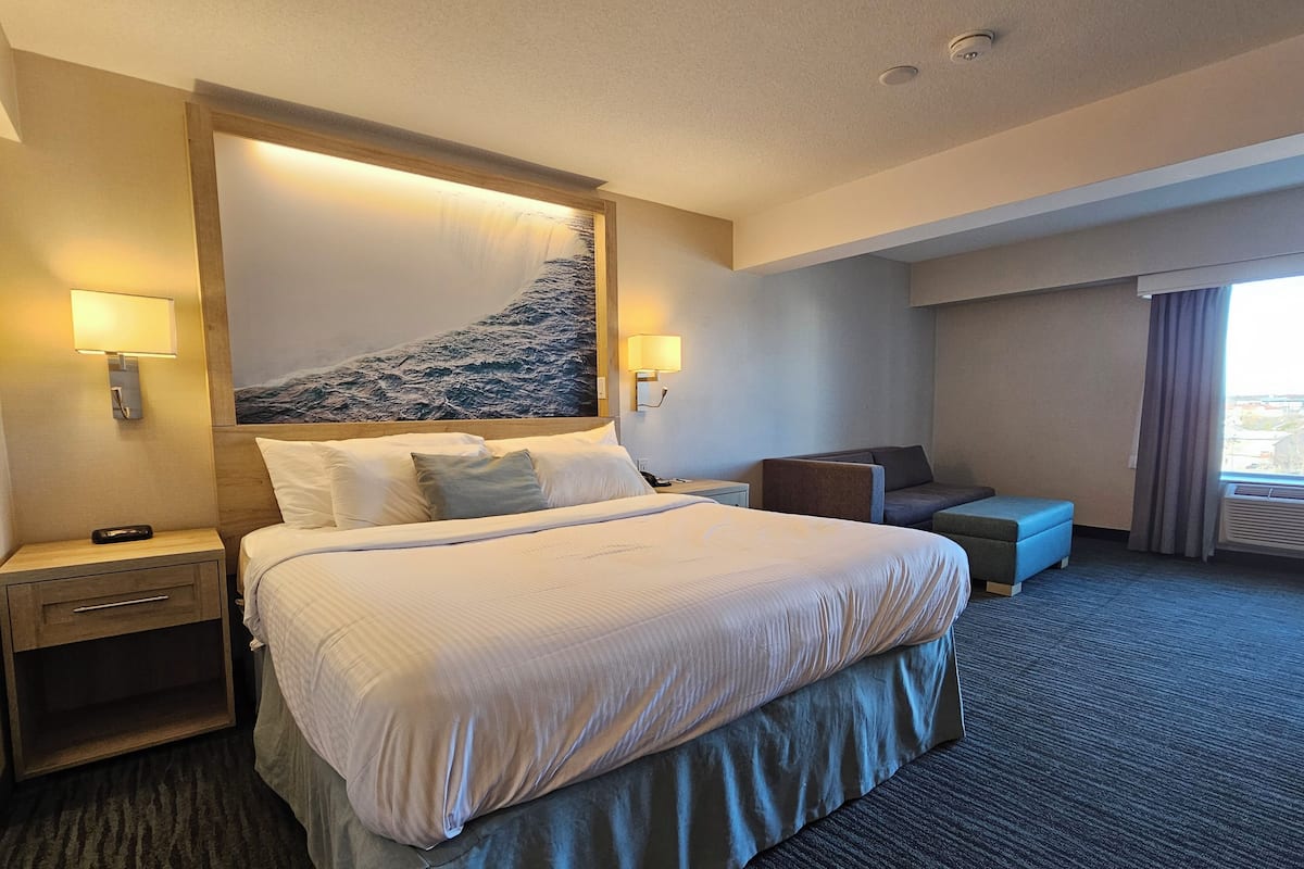Ein Hotelzimmer mit einem großen Bett, zwei Nachttischen, einem Schreibtisch, einem Sessel und einem fenster mit Vorhängen.