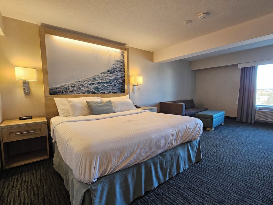 A hotel room with a large bed, two bedside tables, a desk, a chair, and a window with curtains.