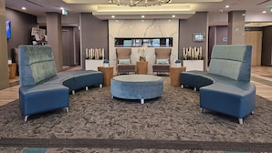 Een lobby met twee blauwe fauteuils, een rond poef, een kroonluchter en een receptiebalie.