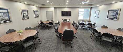 A conference room with a large oval table, multiple chairs, framed pictures on the walls, and a TV mounted on the wall.