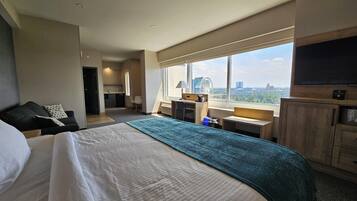 A hotel room with a large bed, a desk, a chair, a TV, and a view of the cityscape.