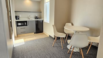 A modern kitchen with a microwave, coffee maker, and kettle, a dining area with a table and chairs, and a carpeted floor.