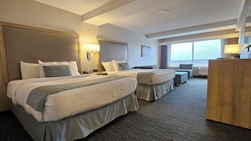 Ein Hotelzimmer mit zwei Betten, einem Schreibtisch, einem Sessel und einem großen Fenster mit Blick auf die Stadt.