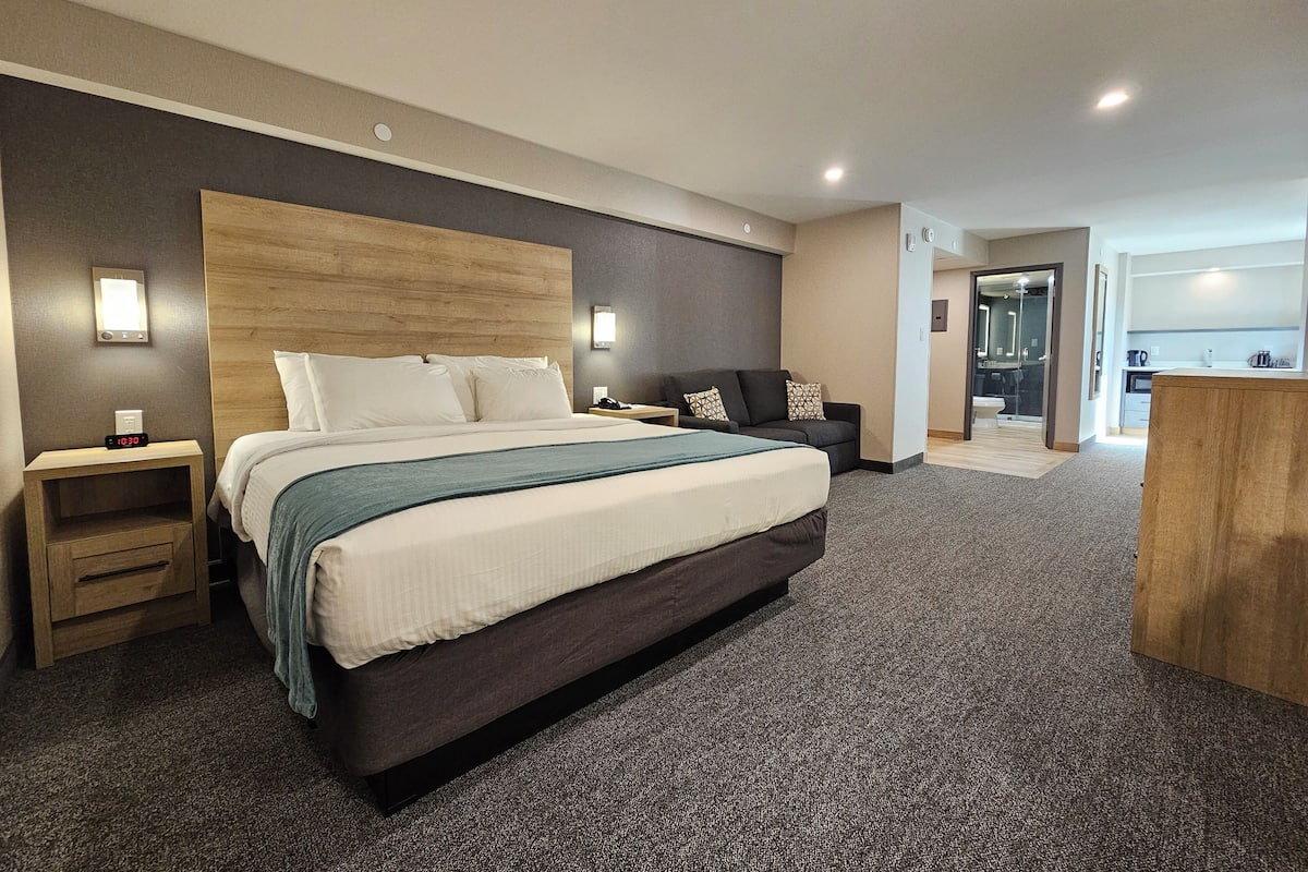 Ein modernes Hotelzimmer mit einem großen Bett, einem Nachttisch, einer Couch und einem Holztisch.