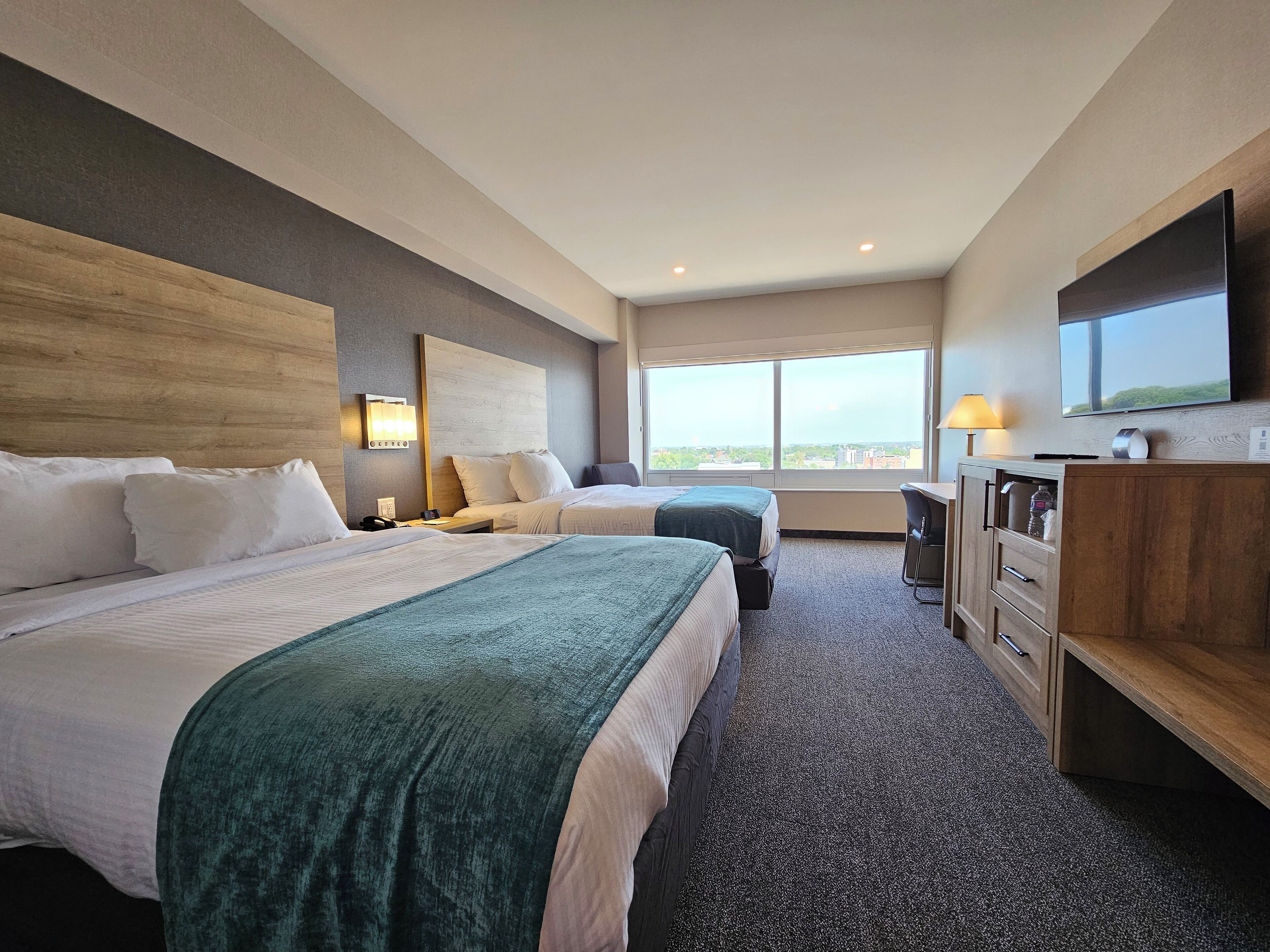 A hotel room with two beds, a desk, a TV, and a large window.