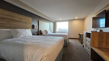 A hotel room with two beds, a TV, a desk, and a window.
