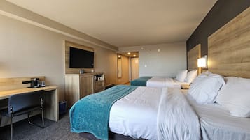 Ein Hotelzimmer mit zwei Betten, einem Schreibtisch, einer Kaffeemaschine, einem Fernseher und einem Spiegel.