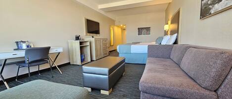 A hotel room with a sofa, a desk, a chair, a TV, and a bed.