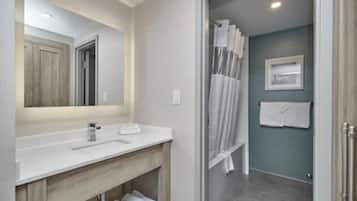 A modern bathroom with a white vanity, a large mirror, a shower with a glass door, and a towel rack.