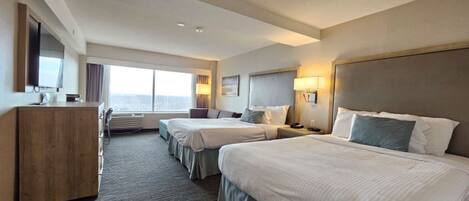 A hotel room with two beds, a desk, and a large window.