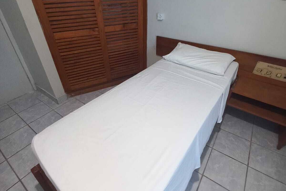 A small, clean room with a single bed, a wooden wardrobe, and a small table.